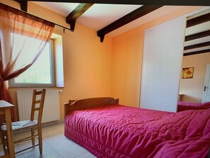 Une chambre à coucher avec un lit, une chaise, une fenêtre avec des rideaux, un radiateur et une porte.