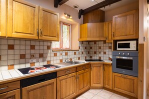Een keuken met houten kastjes, een magnetron, een oven en een vaatwasser.
