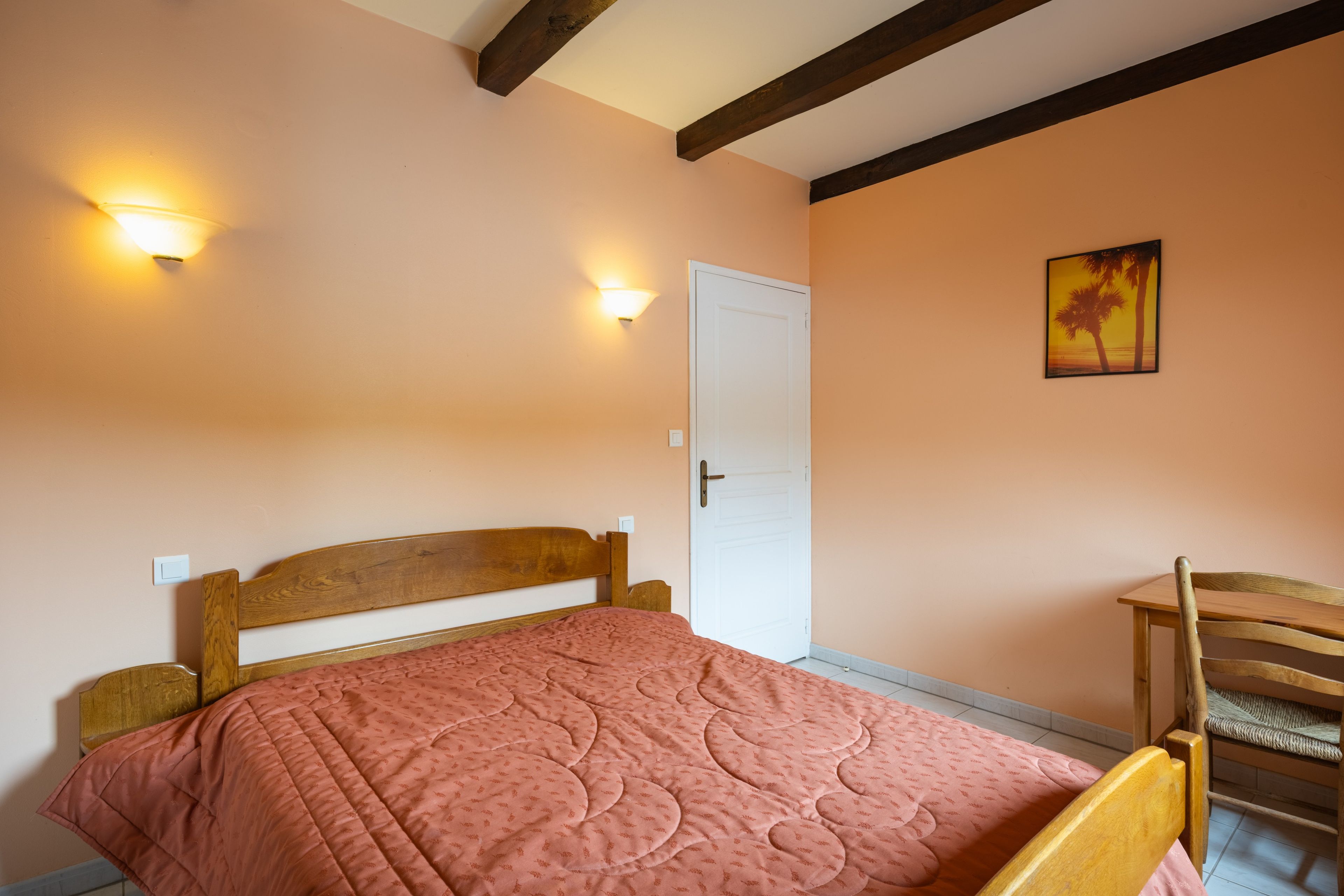 A bedroom with a bed, a chair, a door, and two wall-mounted lights.