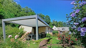 A garden with a pergola, a stone building, and a vintage water wheel.