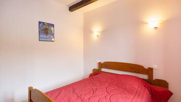A bedroom with a wooden bed, a red bedspread, and two wall-mounted lights.