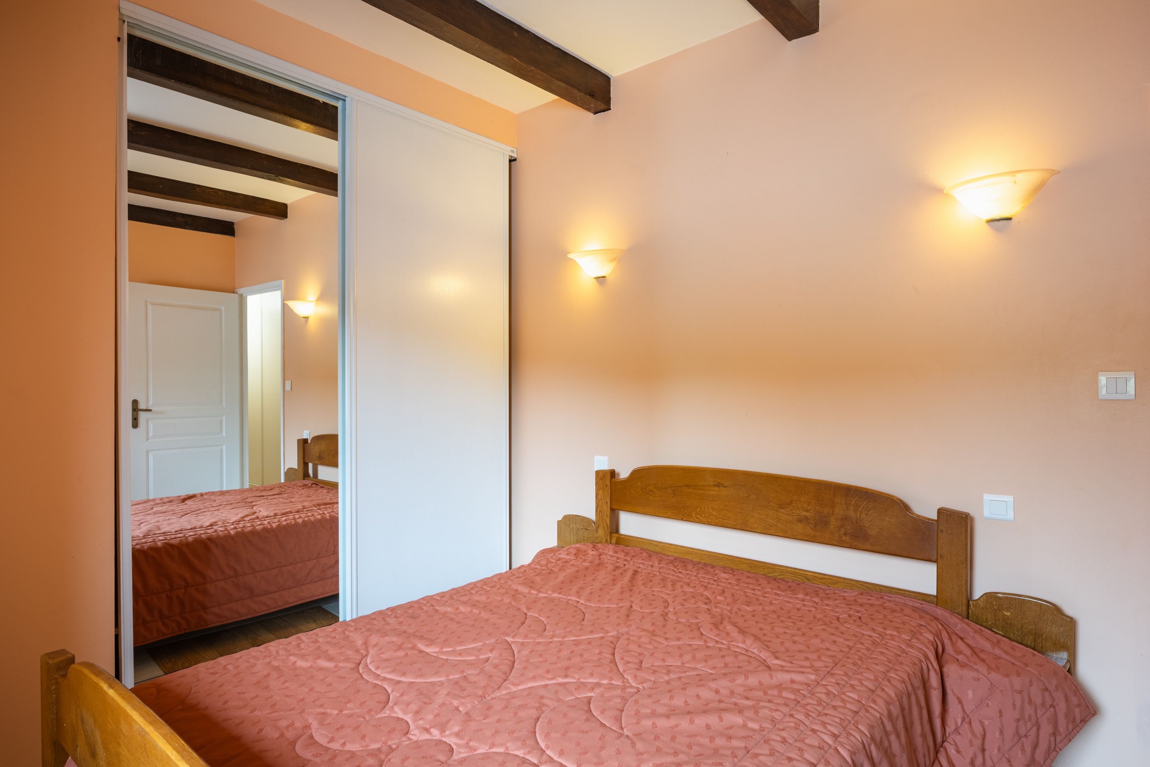 A bedroom with a bed, a door, and two wall-mounted light fixtures.