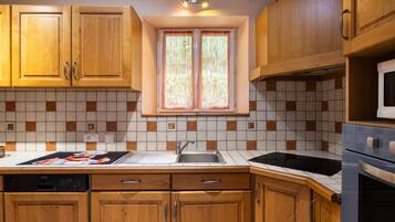 Une cuisine avec des meubles de rangement en bois, un pare-feu en carrelage, une fenêtre avec des rideaux et un four à micro-ondes.