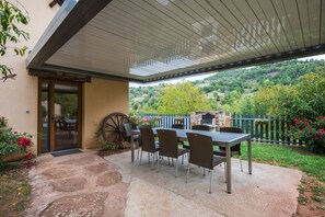 Une terrasse extérieure avec une table et des chaises, une roue en bois et une vue sur une colline.