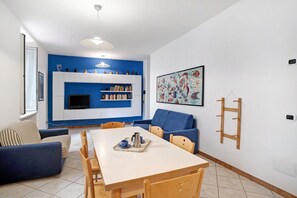 A modern living room with a dining table, blue sofas, a bookshelf, and a TV.