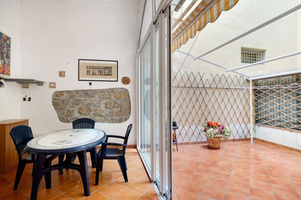 A balcony with a table and chairs, a stone wall, a metal fence, and a potted plant.
