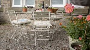 Uma mesa de metal para exterior com cadeiras, uma garrafa de vinho e uma tigela de fruta.