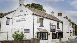 O Wensleydale Heifer, um edifício branco com design tradicional, com sinal de restaurante e bar de peixes, e um letreiro de estacionamento.