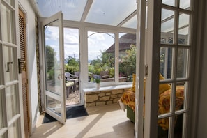 A conservatory with a stone bench, a view of the garden, and a door leading outside. - Church Farm, Wilton, North York Moors (Pickering)
