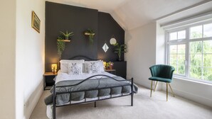 Un dormitorio con cama, mesitas de noche, una silla y un ventanal grande.