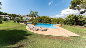 A swimming pool with lounge chairs, surrounded by greenery and a clear sky.