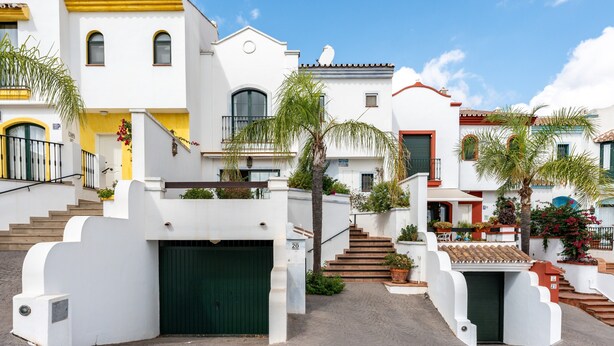 A residential street with white houses, a green garage door, and a staircase leading to a second floor.