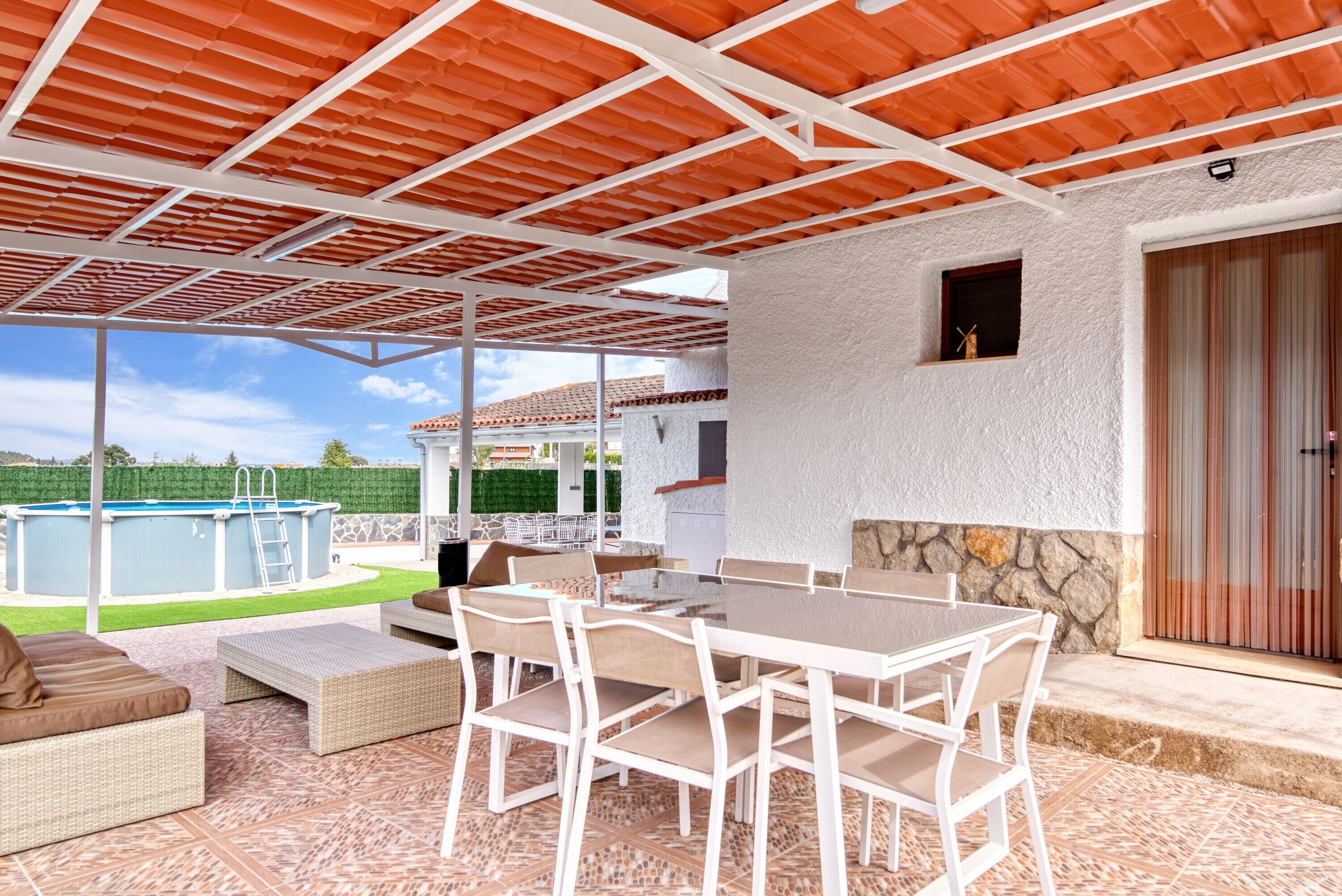 Un patio exterior con piscina, mobiliario de mimbre blanco y una pared de piedra.