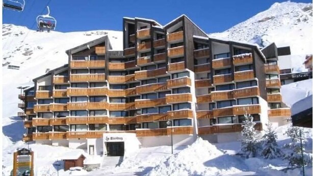 Ein mehrstöckiges Hotel mit Balkonen, ein Skilift im Hintergrund und eine verschneite Berglandschaft.