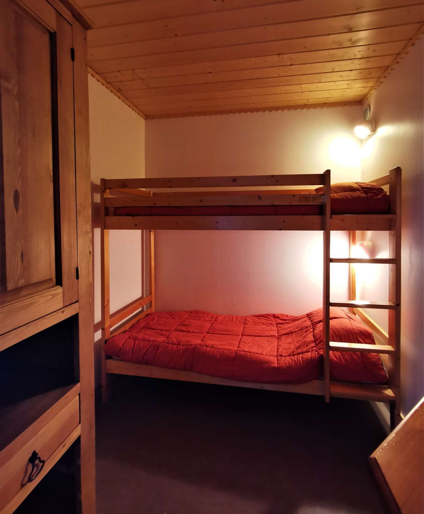 Kerrossängyssä on punainen patja, ja se sijaitsee huoneessa, jonka seinät ja katto ovat puuta.