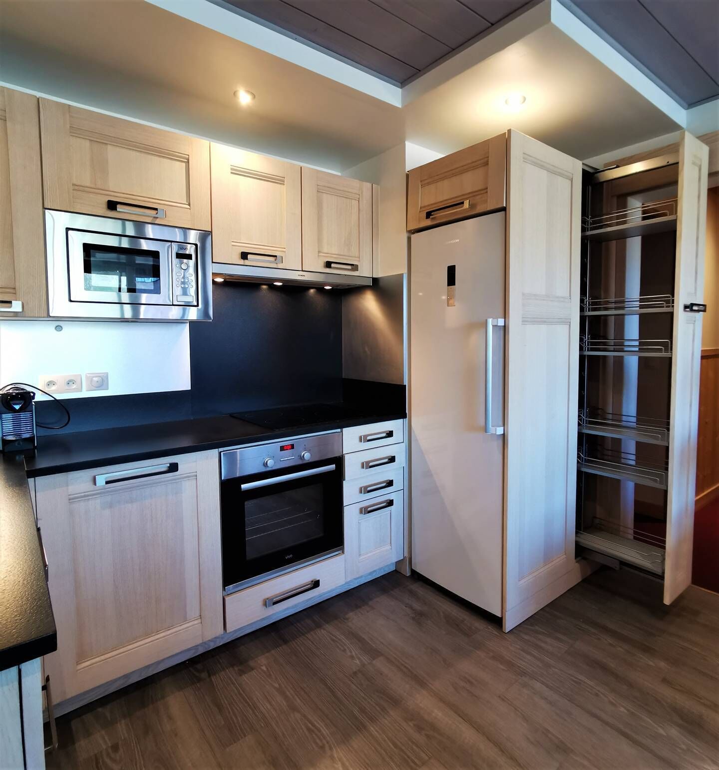 Uma cozinha compacta com micro-ondas, forno e frigorífico, armários de madeira e despensa embutida.