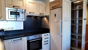Eine kleine Küche mit Mikrowelle, Backofen und Kühlschrank, Holzschränken und einem eingebauten Vorratsschrank.