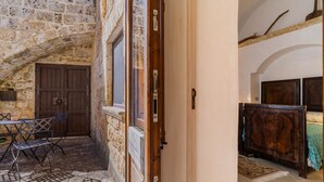 An interior view of a stone building with a wooden door, a small table with chairs, and a tiled floor. - Apartment 'Antica Corte Dell'800' with Private Terrace, Wi-Fi and Air Conditioning (castrignano del capo)