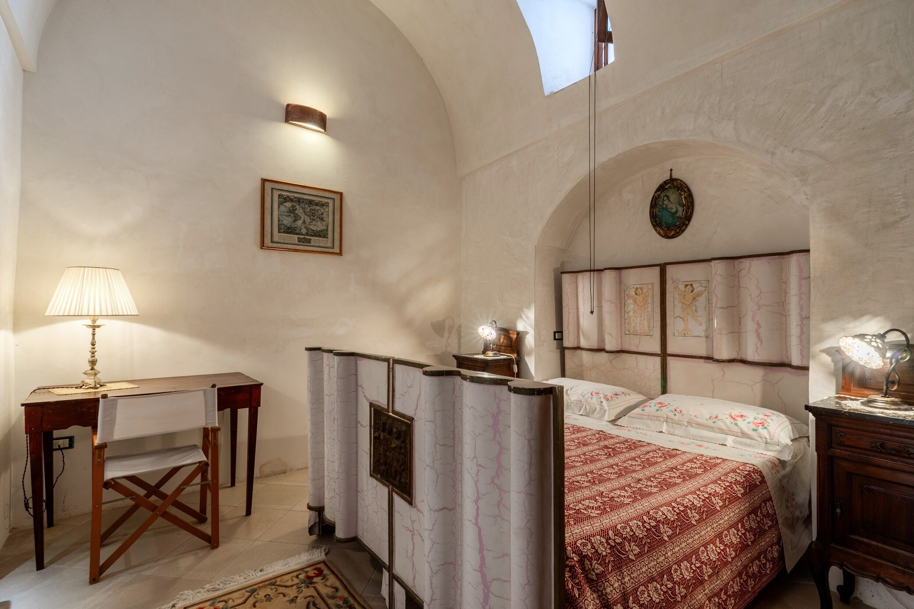 A bedroom with a bed, a desk, a chair, a lamp, and a picture on the wall.