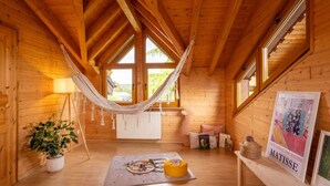 Una habitación acogedora de cabaña de madera con una hamaca, un radiador, una pequeña mesa con un objeto amarillo y un cartel en la pared.