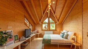 Un dormitorio rústico de cabaña con cama, televisor y ventana con vistas a la vegetación.