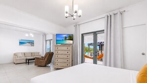 A hotel room with a bed, a sofa, a chair, a TV, and a view of the outdoors. - Luxury 4BR Villa in Tierra del Sol by Bocobay (Noord)