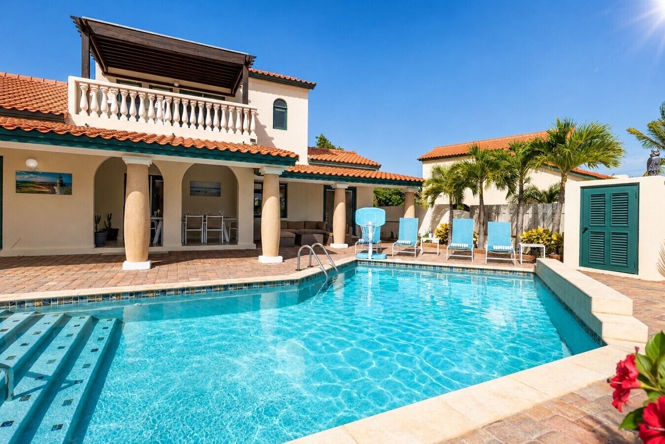 Une piscine avec des chaises longues, un patio couvert et un bâtiment à deux étages doté d’un balcon.