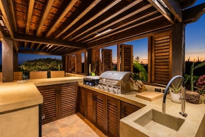 An outdoor kitchen with a grill, a sink, and wooden shutters.