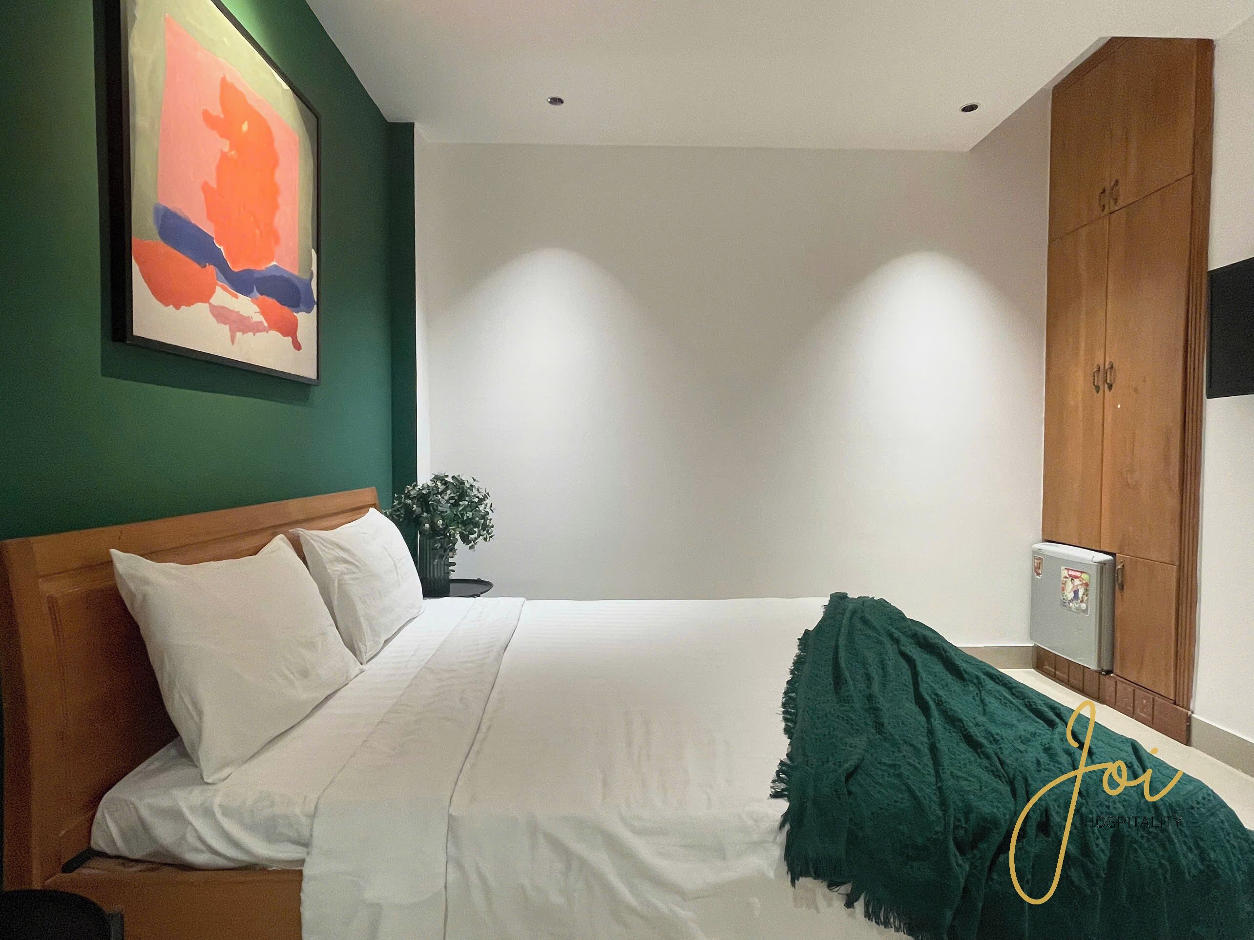 A bedroom with a bed, a nightstand, a plant, and a wardrobe.