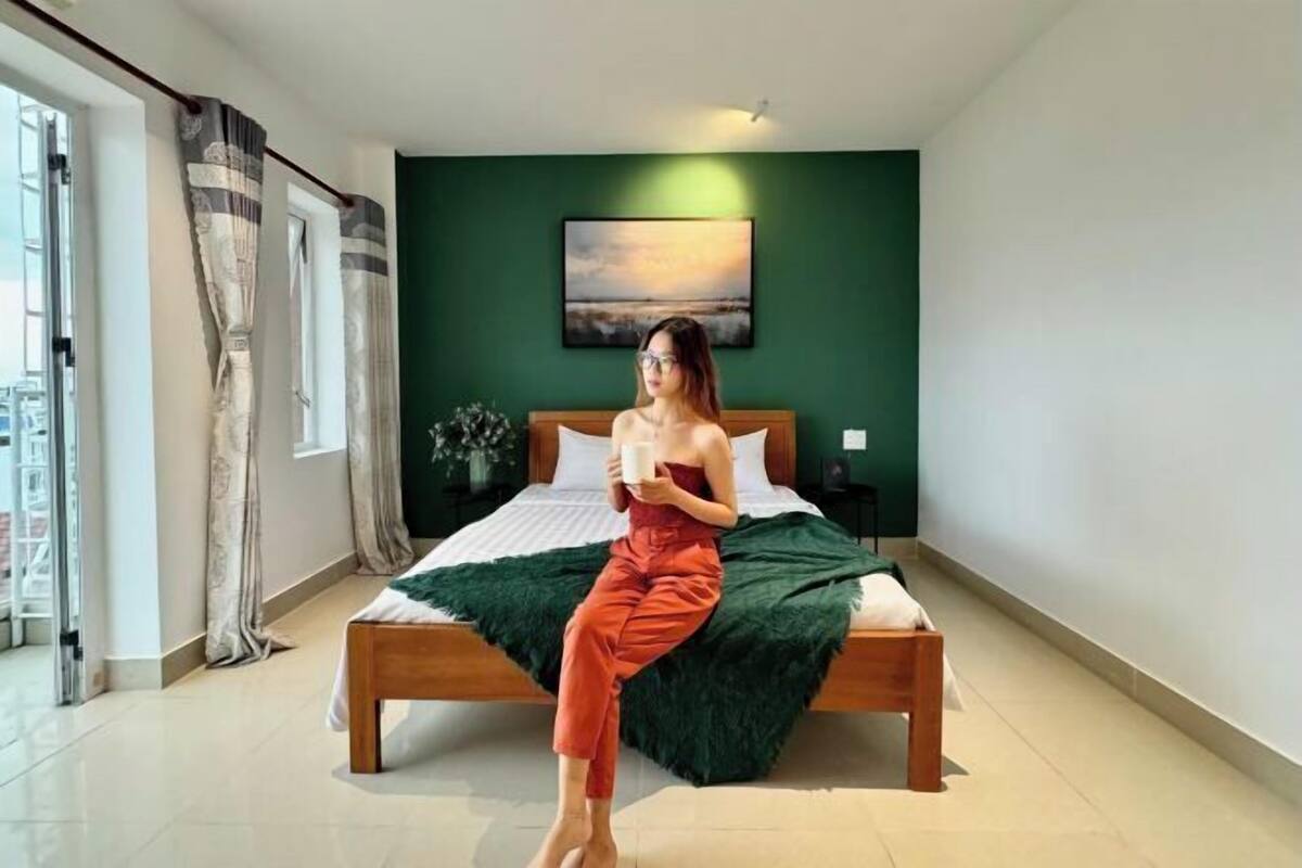 Une chambre à coucher avec un lit, des murs verts, une fenêtre avec des rideaux et un tableau accroché au mur.