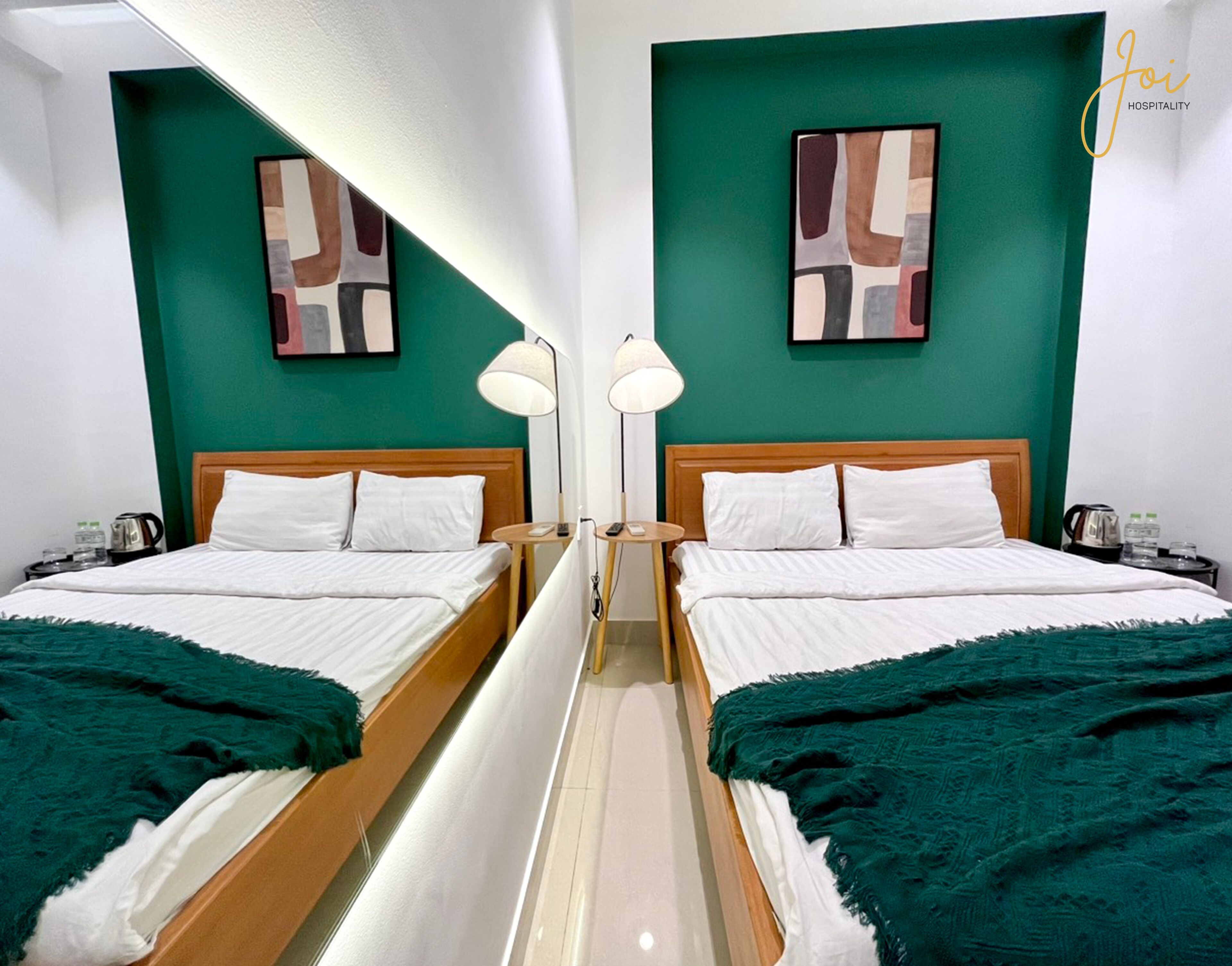 A mirrored room with two beds, green walls, and artwork.