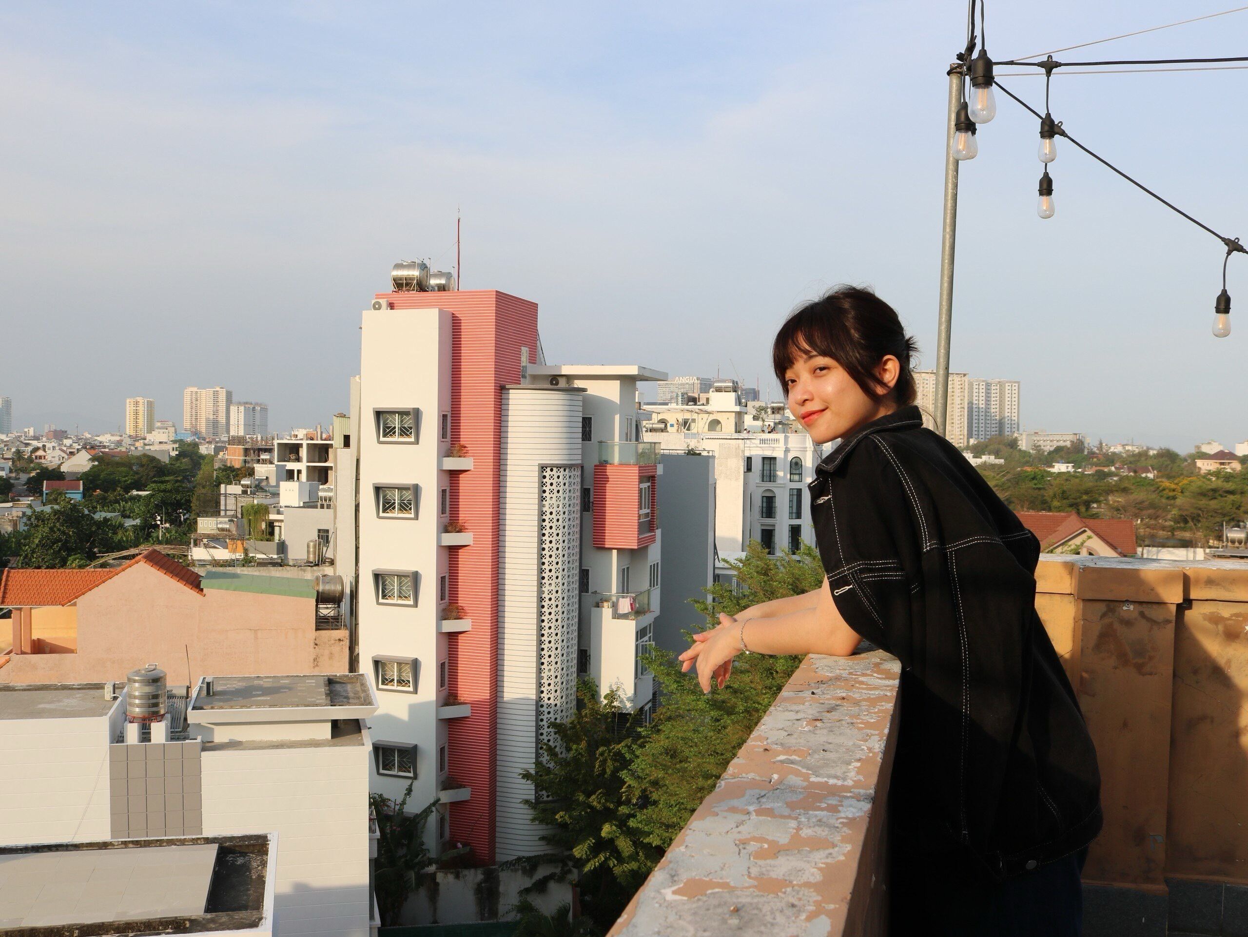 Une personne se tient sur un balcon, d’où elle a une vue sur un paysage urbain avec des bâtiments modernes.