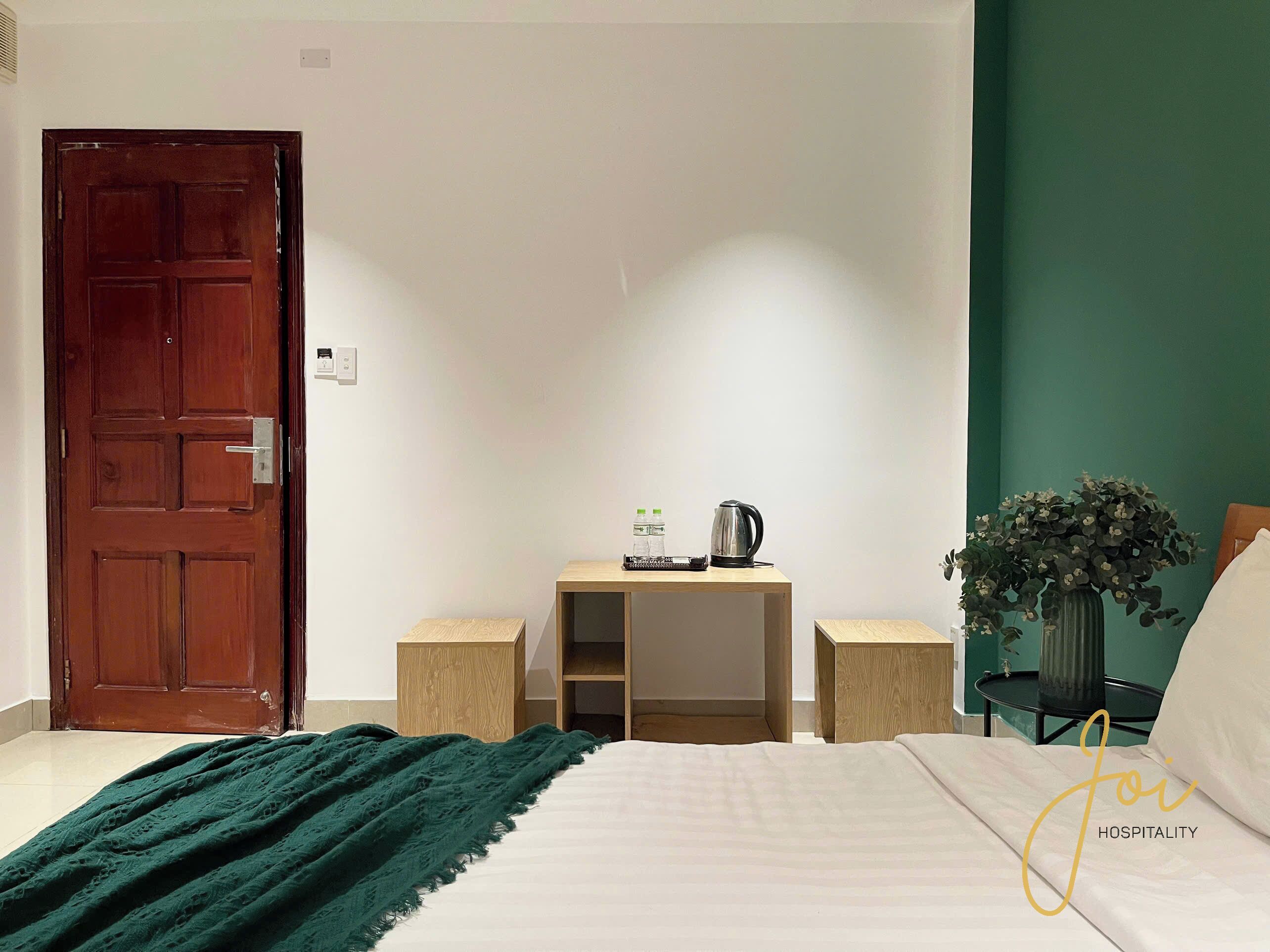 Een slaapkamer met een bed, een houten bureau, een stoel, een groene plant en een deur.