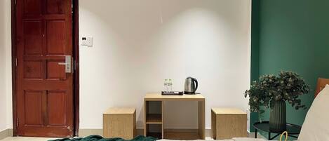 Een slaapkamer met een bed, een houten bureau, een stoel, een groene plant en een deur.