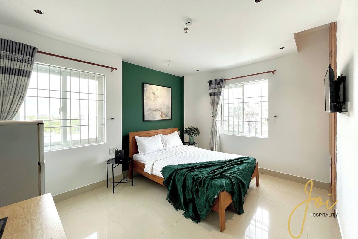 Une chambre à coucher avec un lit, une table de chevet, une fenêtre avec des rideaux et un téléviseur fixé au mur.