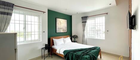 A bedroom with a bed, a nightstand, a window with curtains, and a wall-mounted TV.