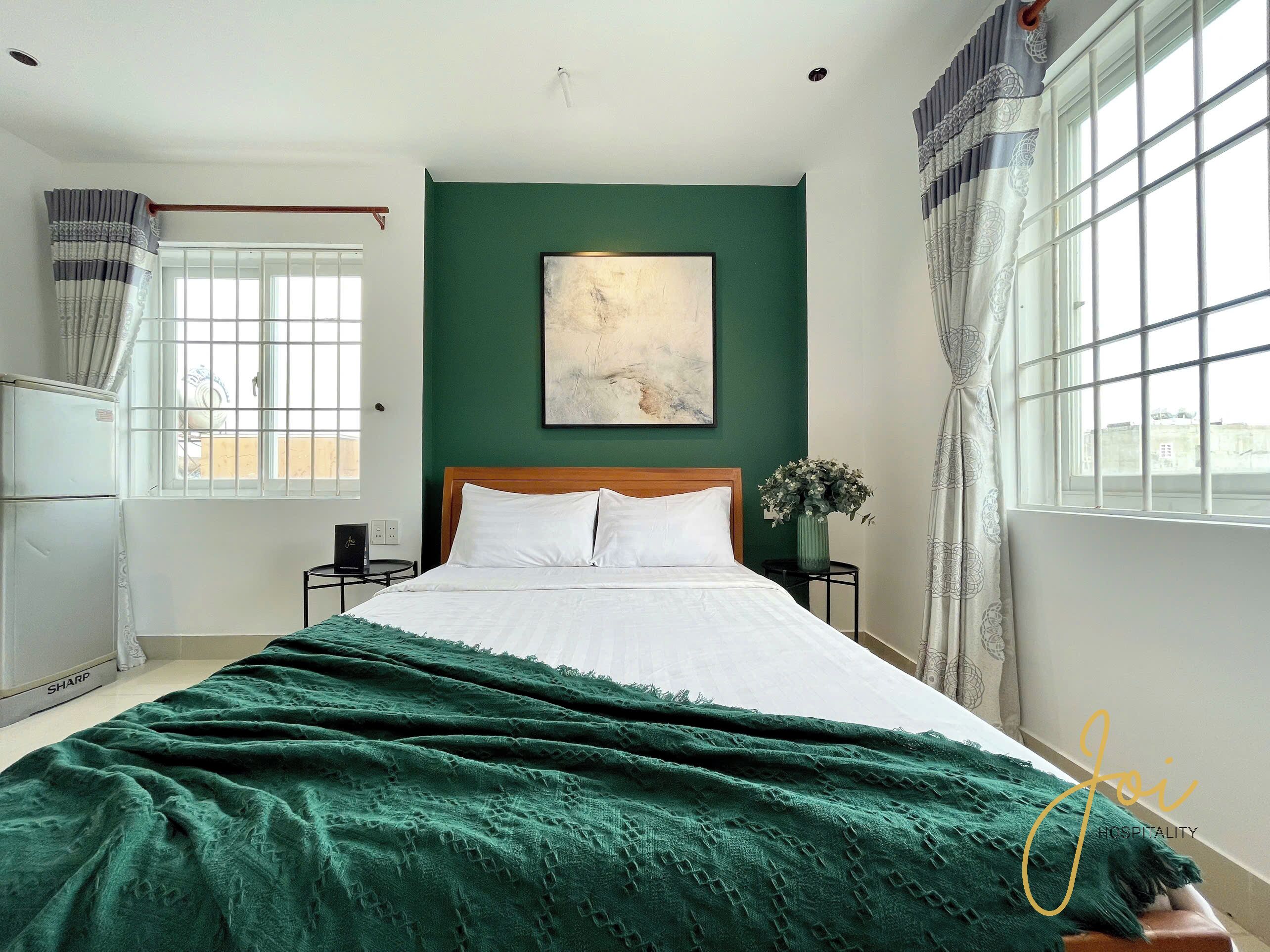 A bedroom with a bed, a nightstand, a window with curtains, a wall-mounted painting, and a green wall.