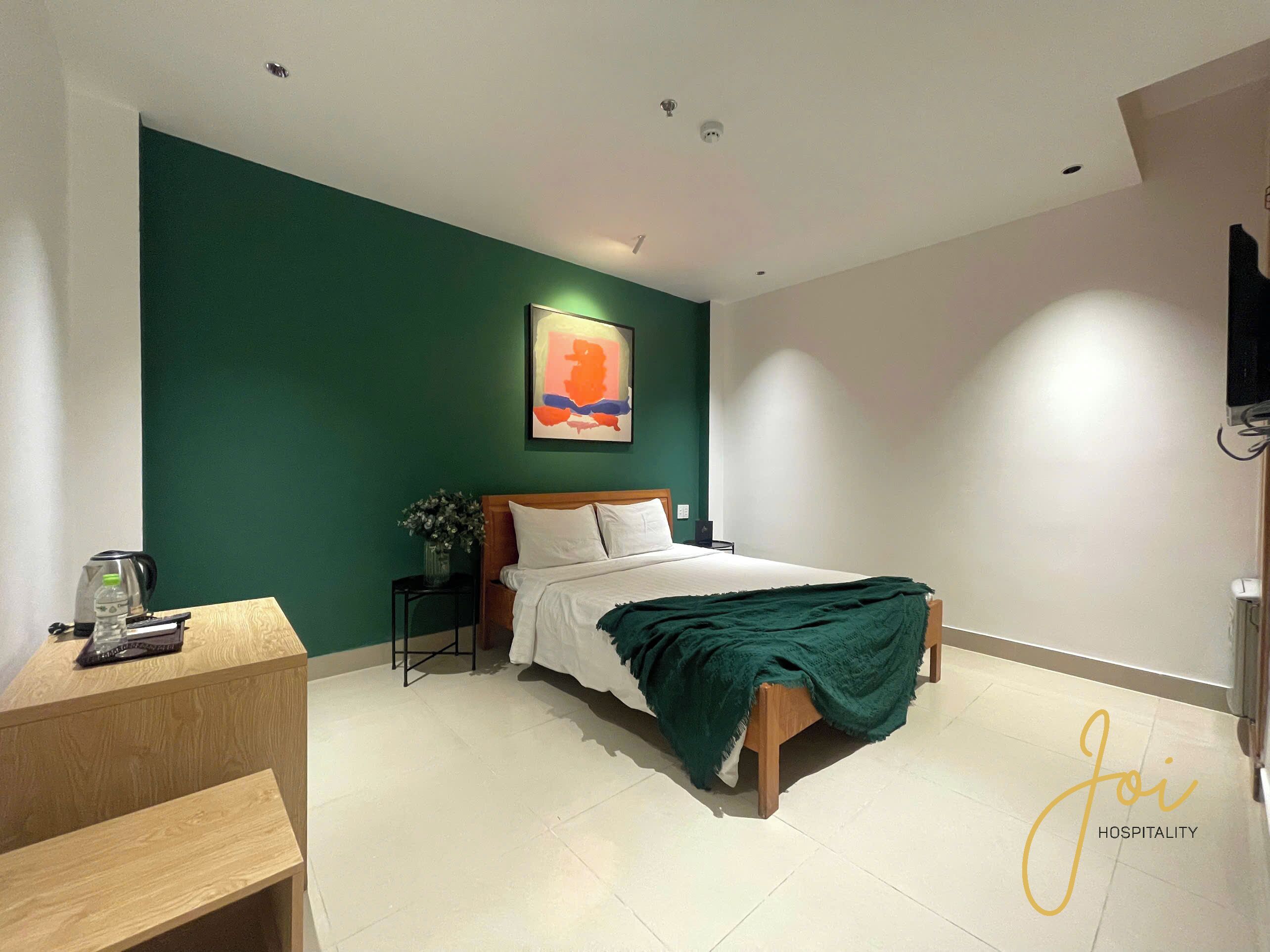 Una habitación de hotel moderna con una cama, una mesita de noche y un cuadro en una pared verde.