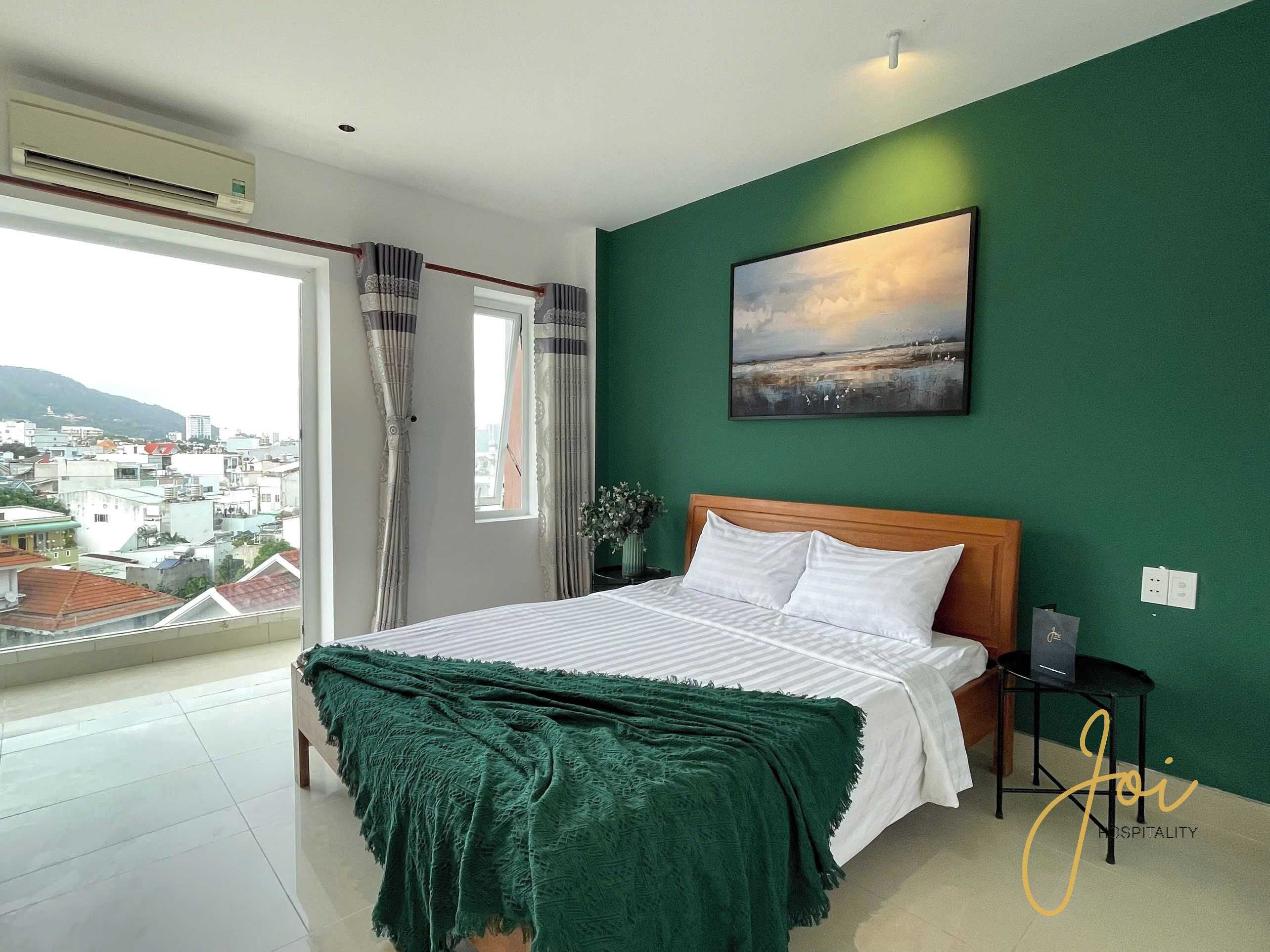 Un dormitorio con cama, pared verde, un cuadro y vistas a la ciudad.