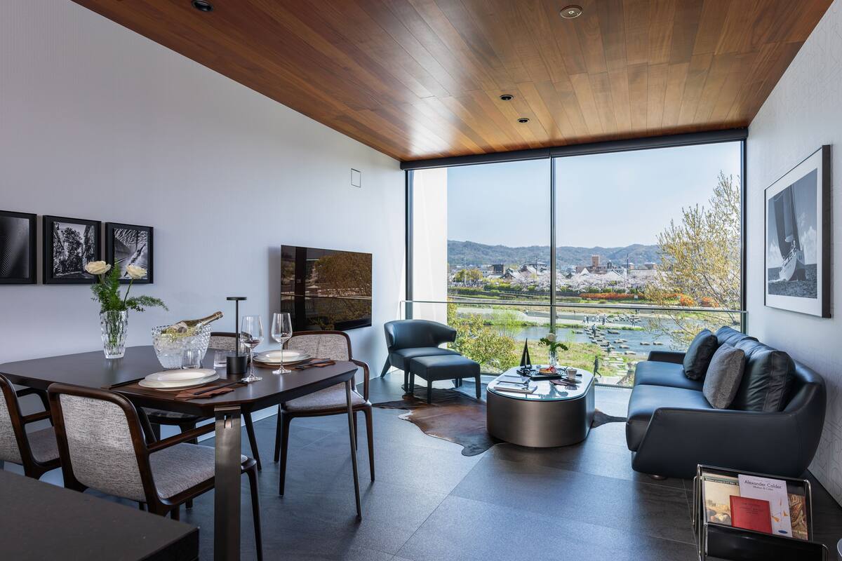 A modern living room with a dining area, large windows, and a view of a cityscape.