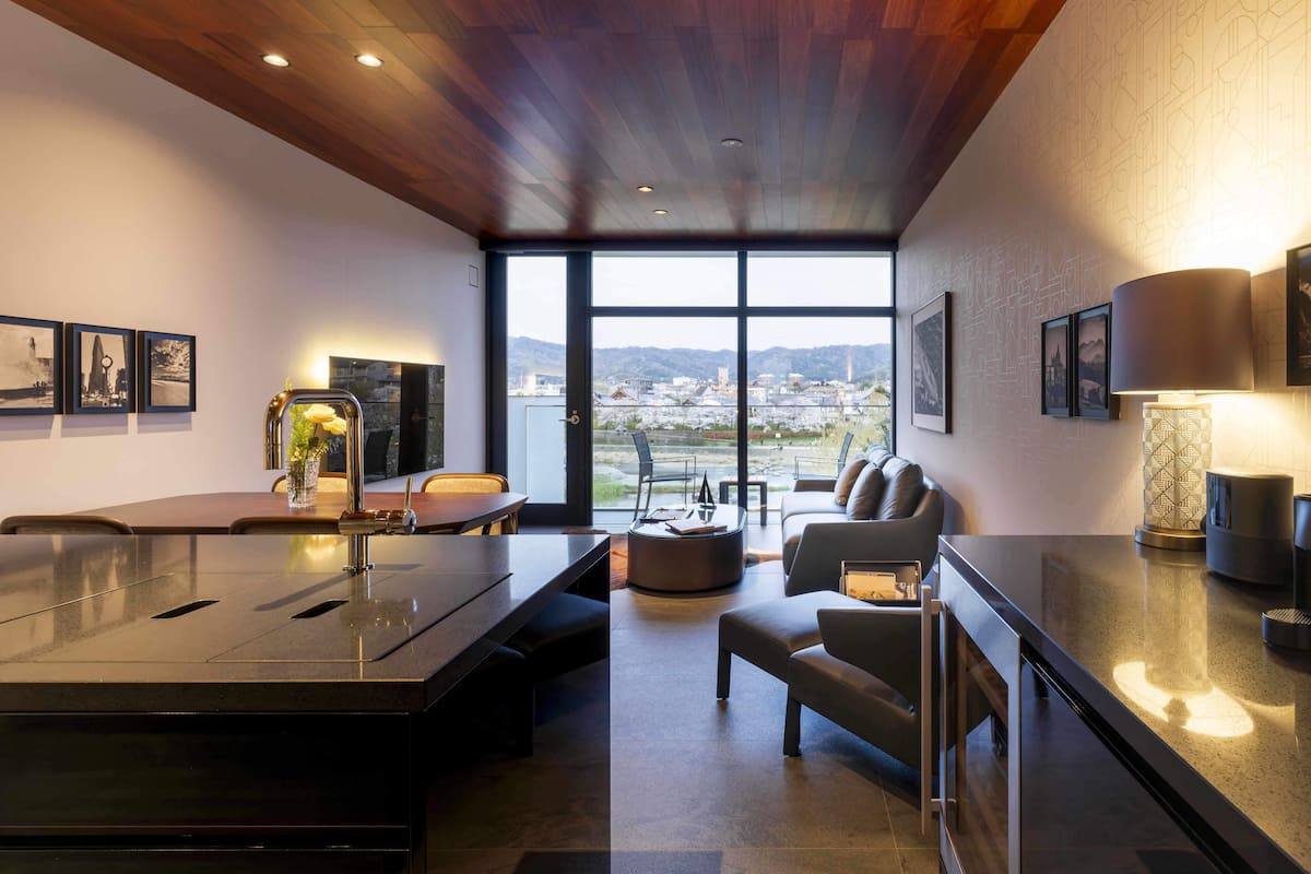 A modern kitchen with a large island, seating area, and large windows offering a city view.