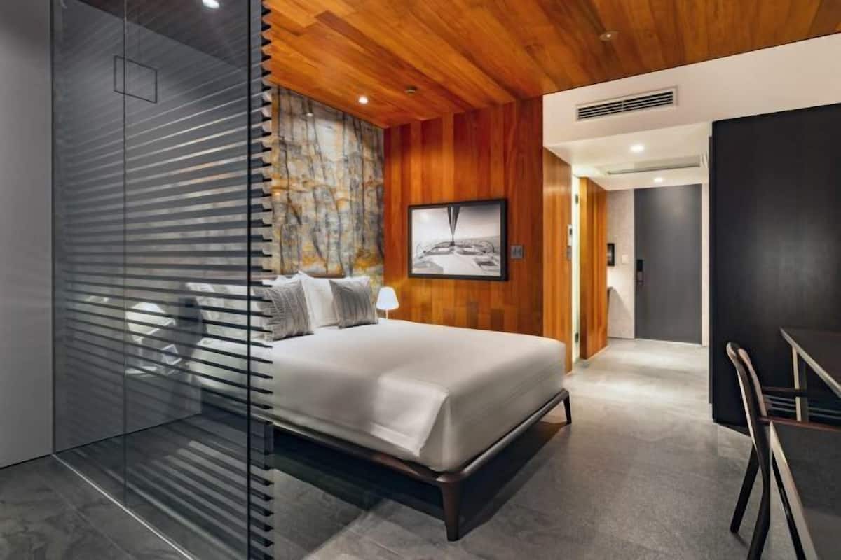 A modern bedroom with a bed, a glass partition, wooden ceiling, and a framed picture on the wall.