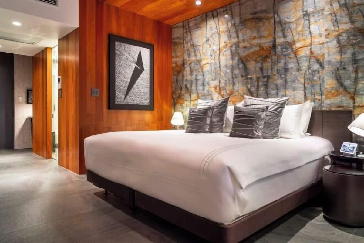 A modern hotel room with a large bed, wooden paneling, a marble wall, and a framed artwork.