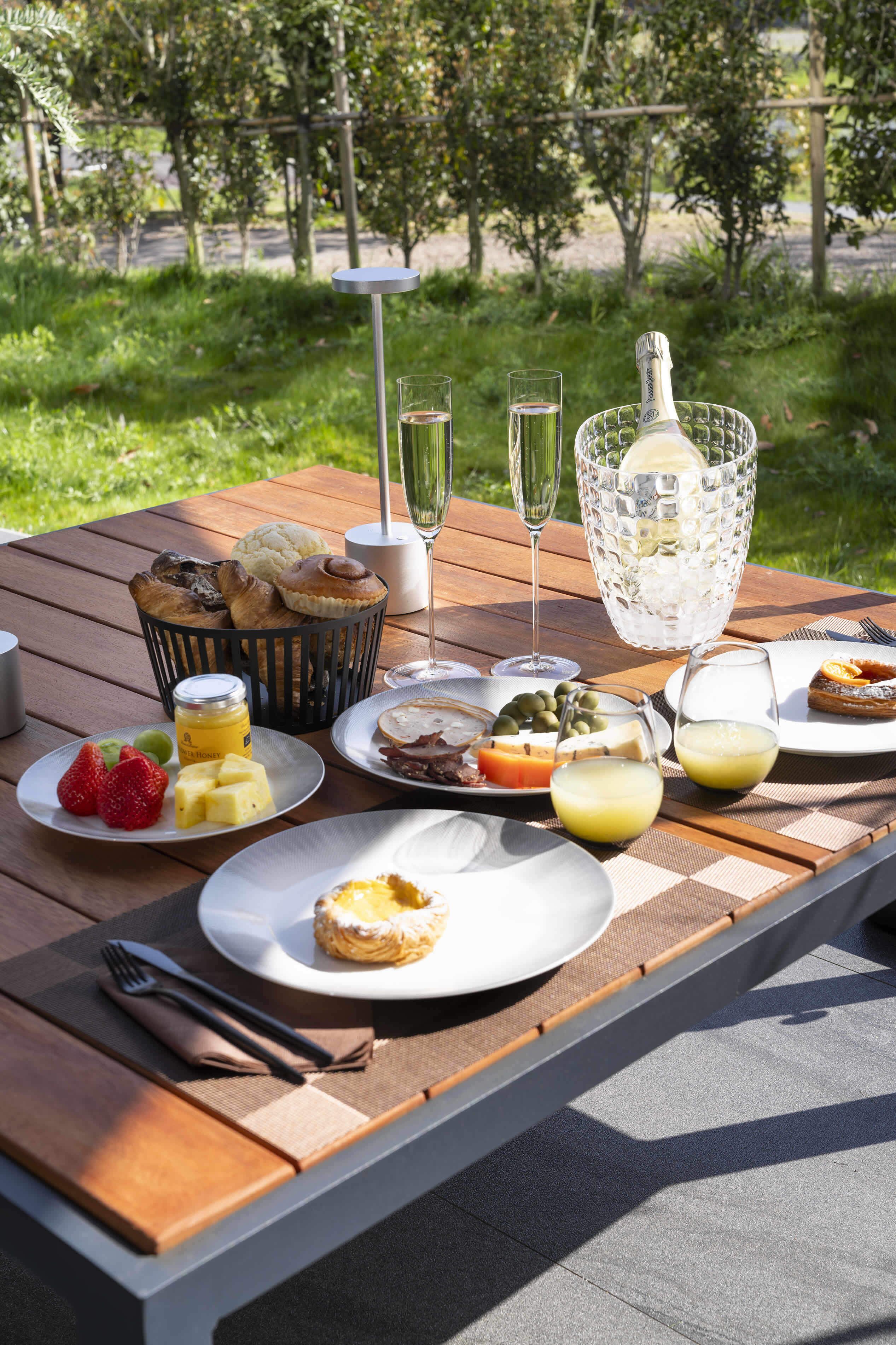 Uma mesa de piquenique ao ar livre com comida, bebidas e uma cesta de doces.