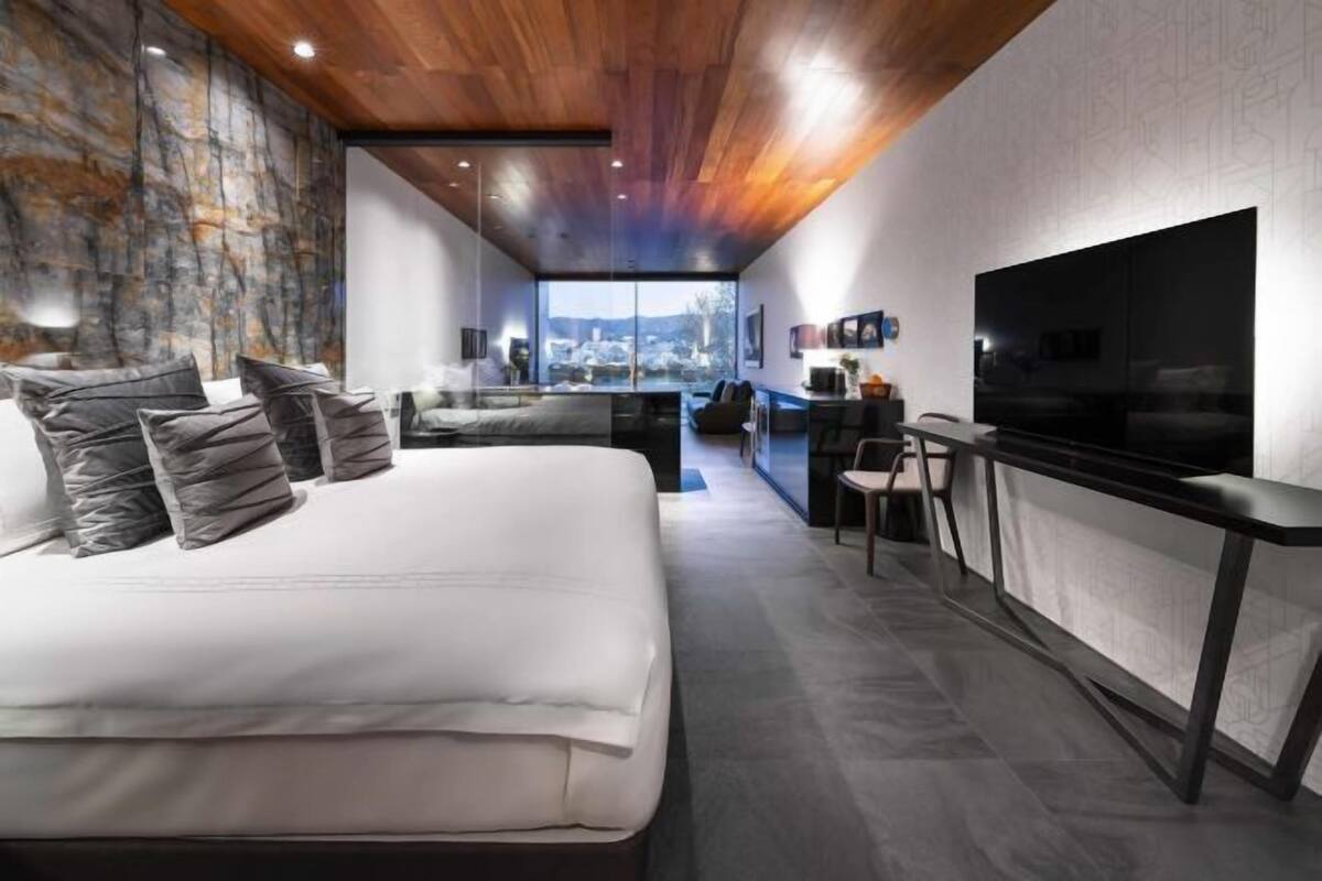 A modern bedroom with a large bed, a desk, and a TV.