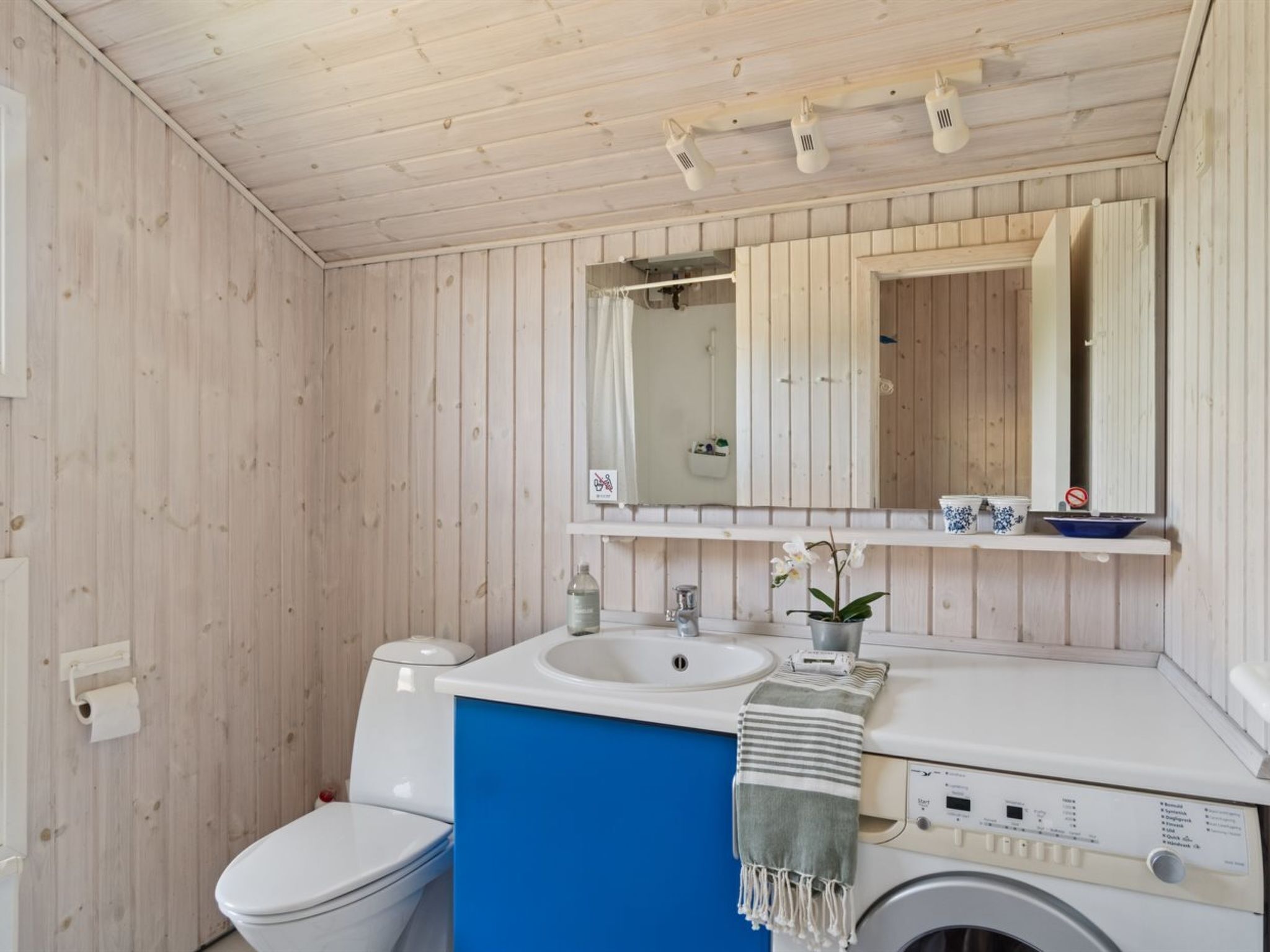 A bathroom with a white toilet, a sink, a mirror, and a washing machine.