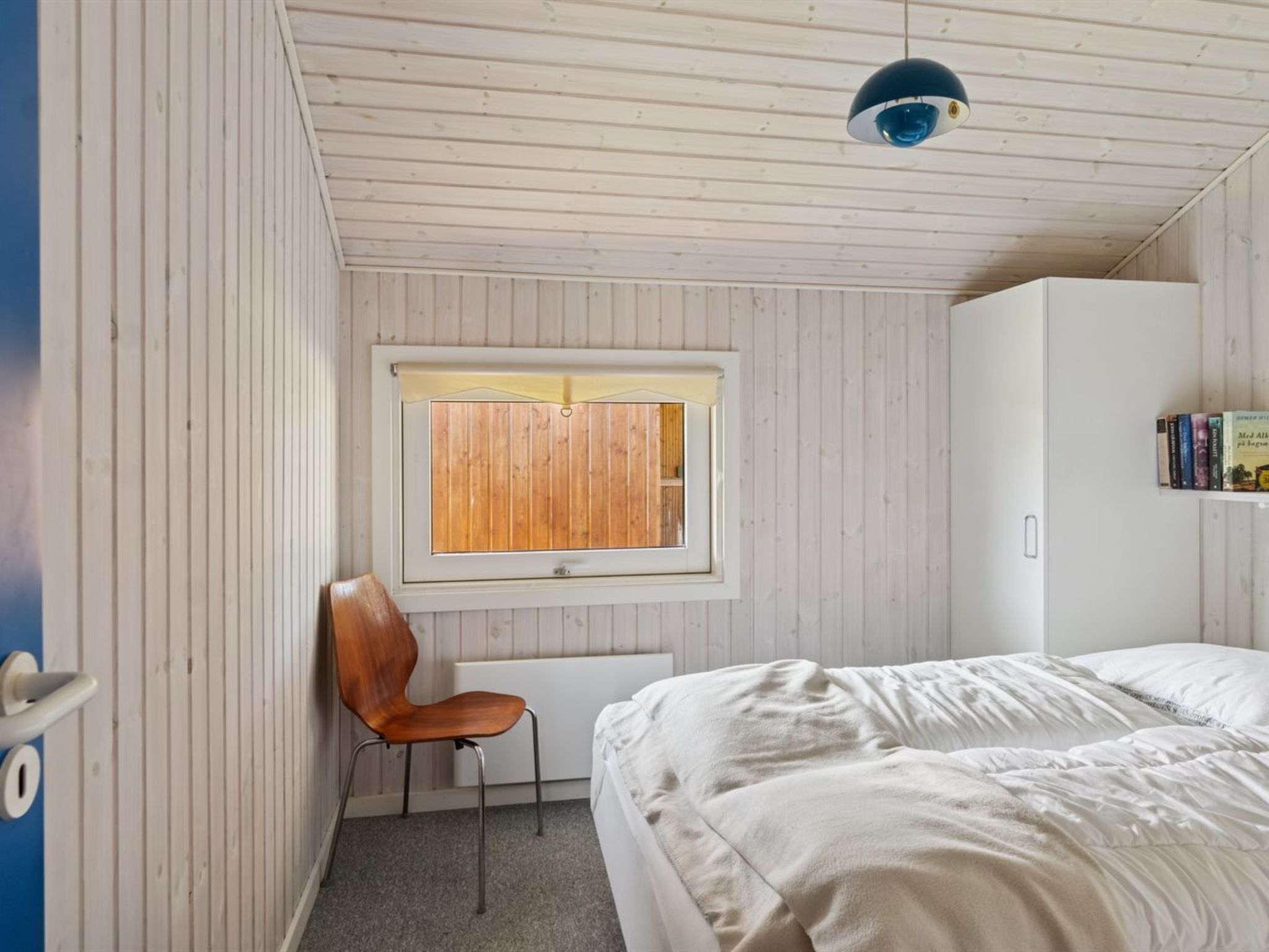 Un dormitorio con cama, una silla, una ventana con persianas y una lámpara en el techo.