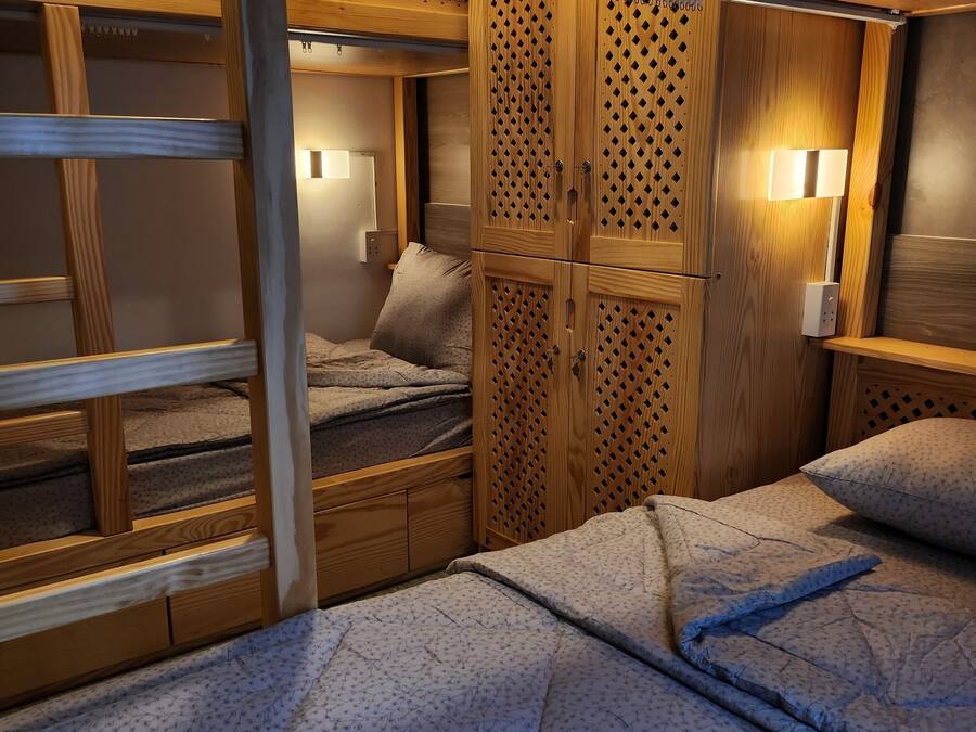 Habitación pequeña y bien iluminada con una cama litera, un armario de madera con diseño de celosía y una mesita de noche con lámpara.