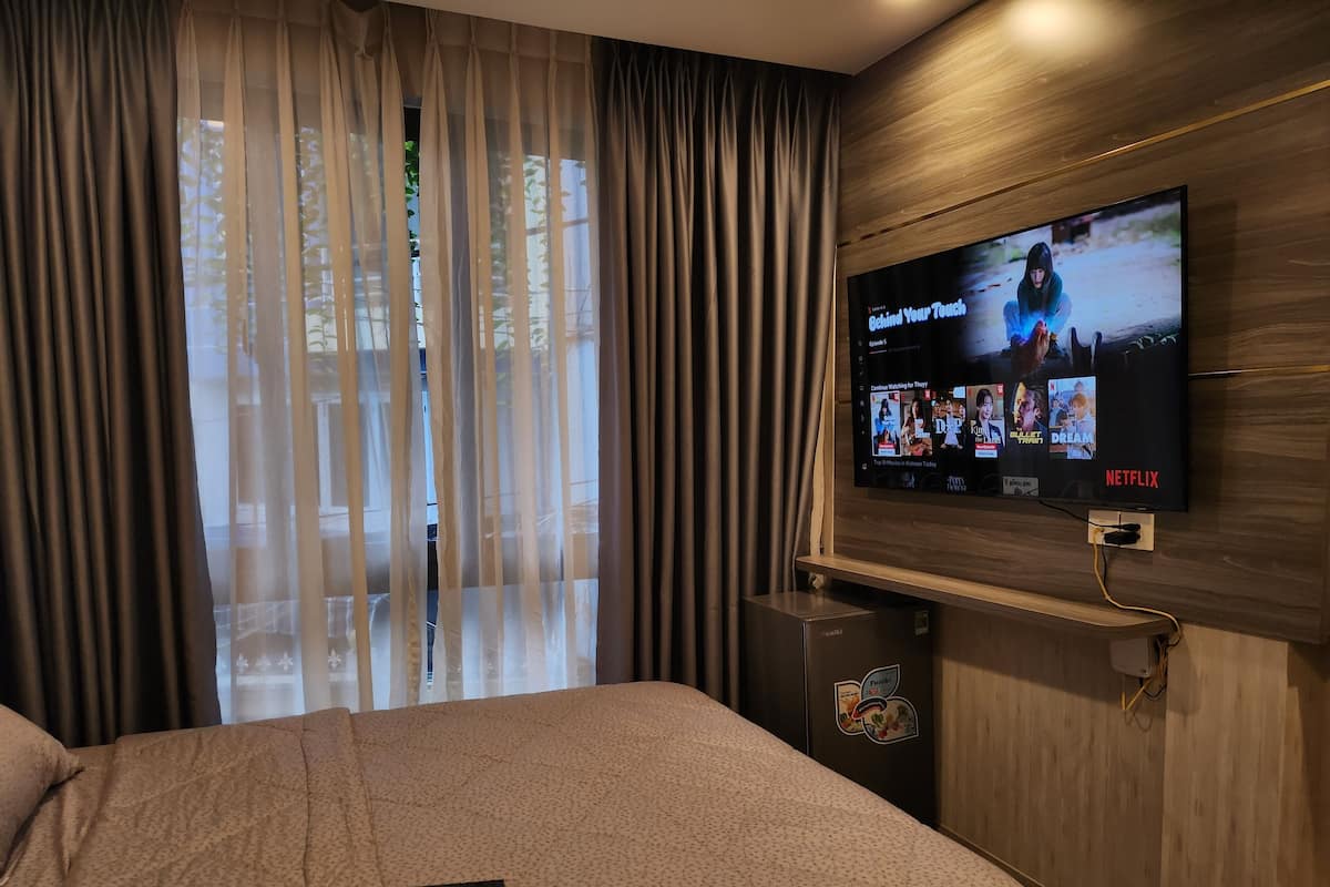 A hotel room with a bed, a TV mounted on the wall displaying Netflix content, and a window with sheer curtains.