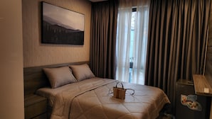 Quarto de hotel com cama, mesa de cabeceira, cômoda, um quadro na parede e uma janela com cortinas.